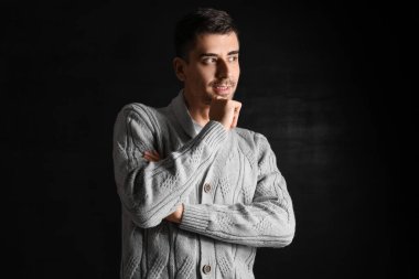 Esmer arka planda örülü süveter giyen yakışıklı bir genç.