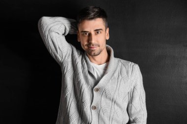 Esmer arka planda örülü süveter giyen yakışıklı bir genç.