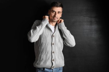 Esmer arka planda örülü süveter giyen yakışıklı bir genç.