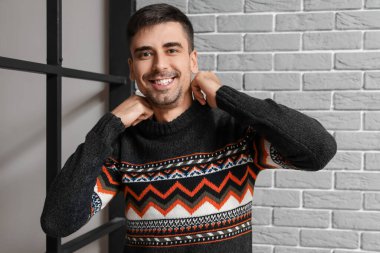 Gri tuğla duvarın yanında örülü süveter giyen yakışıklı bir genç.