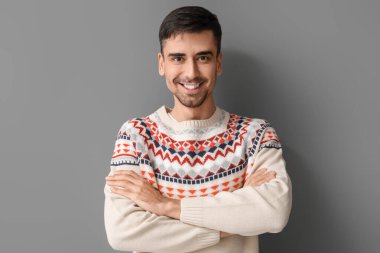 Gri arka planda örülü süveter giyen yakışıklı genç adam.