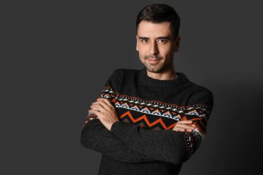 Esmer arka planda örülü süveter giyen yakışıklı bir genç.