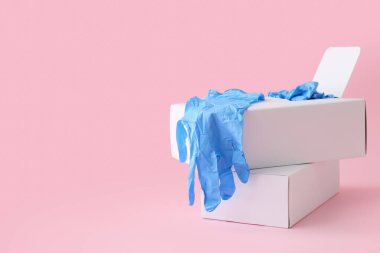 Pembe arka planda tıbbi eldivenli karton kutular.