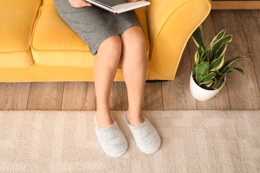 Evde rahat terlikler içinde kitap okuyan genç bir kadın.