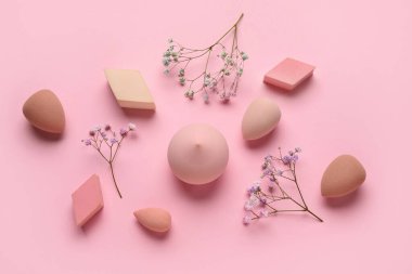 Farklı makyaj süngerleri ve pembe arka planda çiçekler.