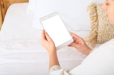 Evde elinde boş ekranlı tablet bilgisayarı olan bir kadın var.