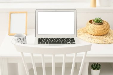 Boş ekranlı dizüstü bilgisayar, ışık duvarının yanındaki masada fincan ve çerçeve.