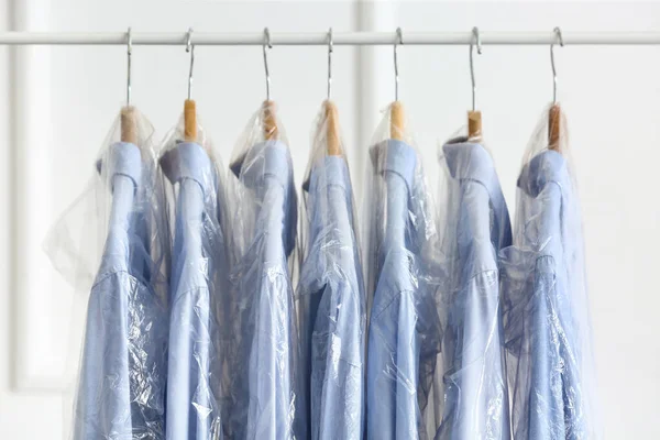 Rack Met Schone Shirts Plastic Zakken Buurt Van Lichte Muur — Stockfoto