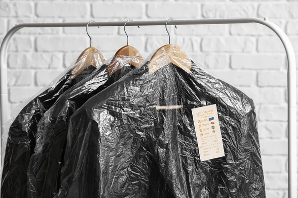 Rack Clean Black Jackets Plastic Bags White Brick Background Closeup — Stock Photo, Image
