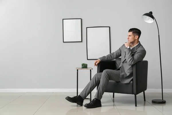 灰色の壁に対して肘掛け椅子に座っている正式なスーツのハンサムな男 — ストック写真