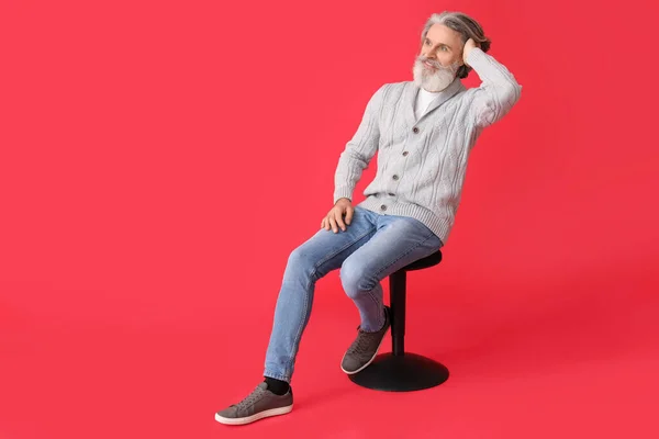 Bonito Homem Sênior Camisola Malha Sentado Cadeira Contra Fundo Vermelho — Fotografia de Stock