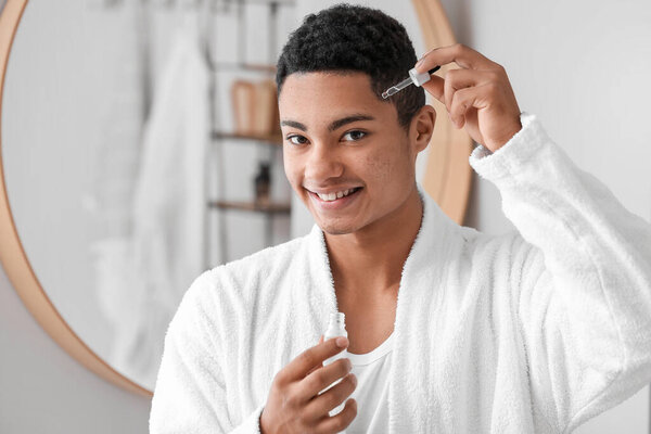 Young African-American guy using serum for skin care in bathroom