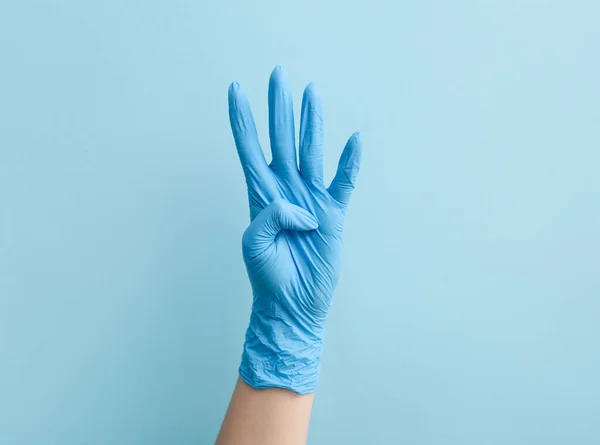 青い背景に4本の指を示す医療手袋の女性医師 — ストック写真
