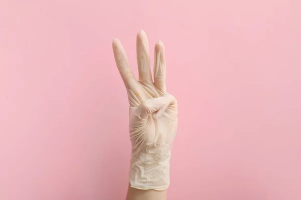 ピンクの背景に3本の指を示す医療用手袋の女性 — ストック写真