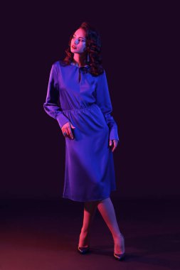 Şık giyinmiş zarif bir kadın koyu arkaplana bakıyor.