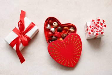 Kalp şeklinde bir kutu, lezzetli çikolata şekerlemeleri ve beyaz arka planda hediyeler.