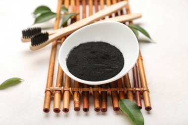 Beyaz arka planda aktif kömür diş tozu ve diş fırçası olan bir kase.