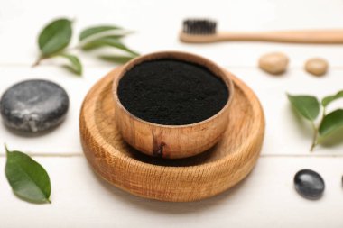 Beyaz ahşap arka planda aktif kömür diş tozu olan bir kase.