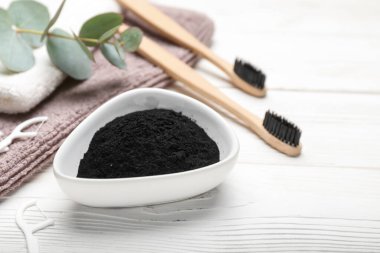 Beyaz ahşap arka planda aktif kömür diş tozu olan bir kase.