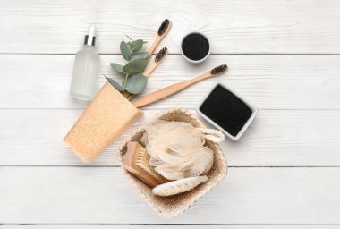 Aktif hale getirilmiş mangal kömürü diş tozu, fırça ve banyo aksesuarları beyaz ahşap arka planda.