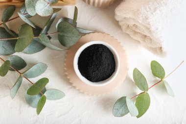 Aktif kömür diş tozu ve beyaz arka planda okaliptüs dalları olan bir kase.