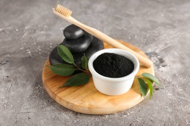 Aktif kömür diş tozu ve gri arka planda taşlar olan kase.