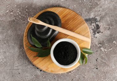 Aktif kömür diş tozu ve gri arka planda taşlar olan kase.