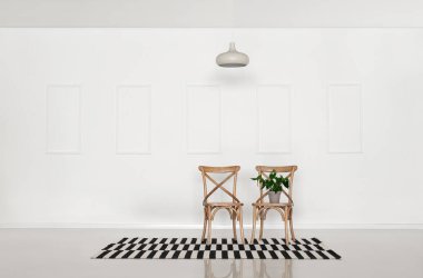 Işık duvarının yanında çiçek, halı ve asılı lamba olan sandalyeler.