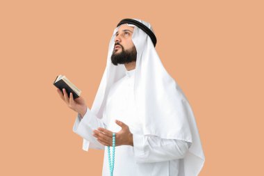 Kur 'an ve boncuklu Müslüman bir adam renkli arka planda dua ediyor.