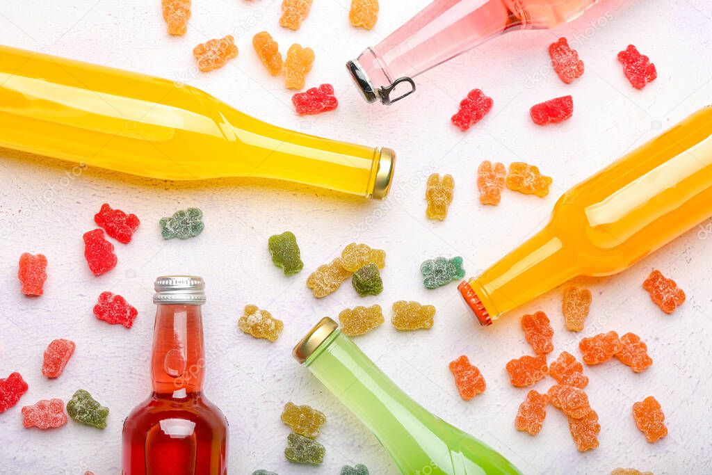 Bottles of drink and different jelly bears on light background