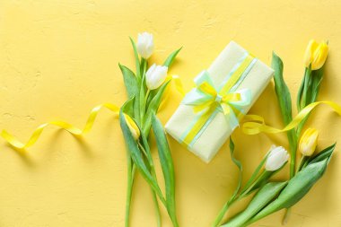Sarı zemin üzerinde Uluslararası Kadınlar Günü için güzel lale çiçekleri ve hediye kutusu