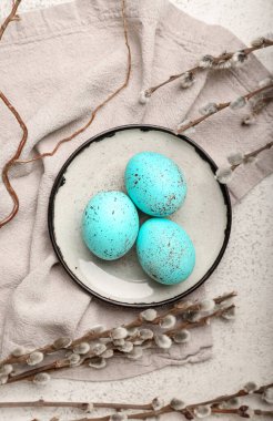 Composition with plate of beautiful Easter eggs and pussy willow branches on light background