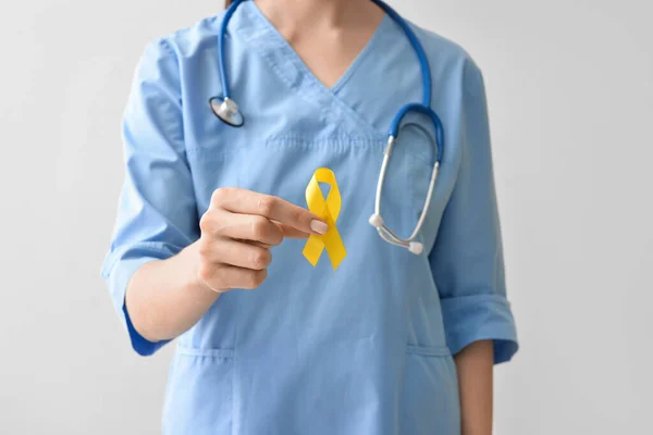 女性看護師光の背景に黄金の意識リボンを保持し クローズアップ 国際小児がんデー — ストック写真
