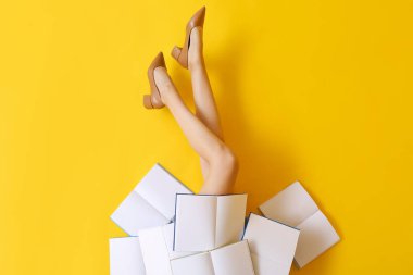 Yaratıcı kompozisyon, boş kitaplar ve sarı arka planda kadın bacakları.