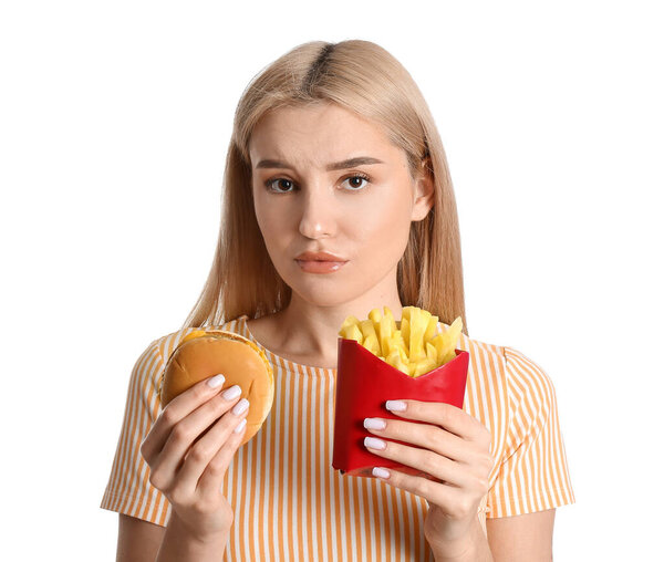 Stressed young woman with french fries and burger on white background