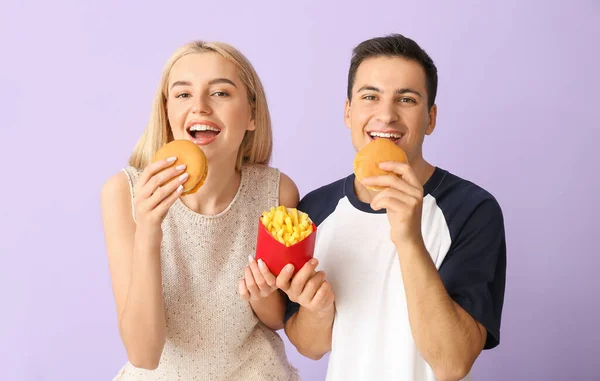 若いですカップルともにフライドポテト食べるハンバーガー紫色の背景 — ストック写真