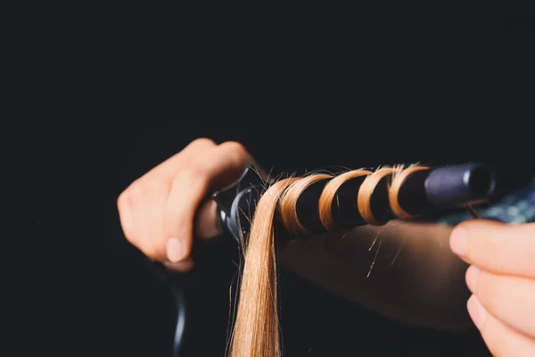 Woman curling hair with modern curler on dark background, closeup