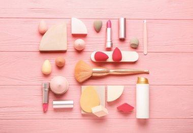 Renkli ahşap arka planda farklı makyaj süngerleri ve kozmetik ürünleri içeren kompozisyon