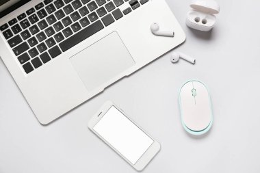 Modern dizüstü bilgisayar, cep telefonu, kulaklık ve beyaz arka planda bilgisayar faresi, yakın plan