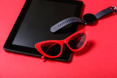 Tablet bilgisayar, akıllı saat ve kırmızı arkaplanda güneş gözlüğü, yakın plan