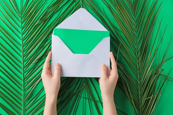 Frauenhände Mit Karte Umschlag Und Palmblättern Auf Grünem Hintergrund — Stockfoto