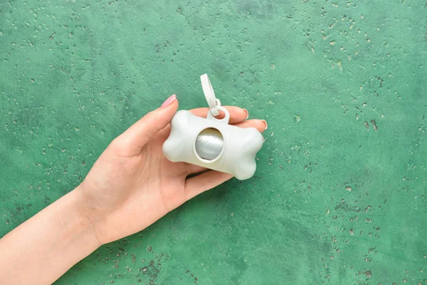 Female hand with pet waste bags on green background, closeup