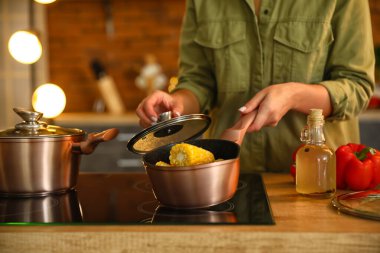 Elinde mısır koçanıyla sos kabı tutan ve mutfakta esrar kapağı açan bir kadın.