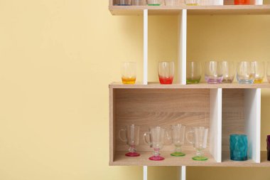 Renk duvarının yanındaki ahşap raf ünitesinde bir sürü farklı bardak var.