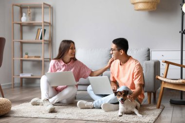 Evde dizüstü bilgisayar kullanan sevimli köpekli genç bir çift.