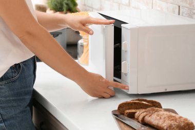 Kadın mutfakta mikrodalga fırın açıyor.
