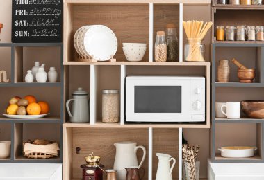 Mutfak aletleri ve modern mikrodalga fırını olan raf ünitesi.