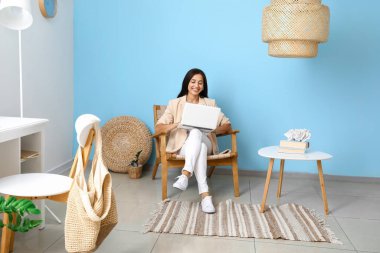 Evdeki tahta koltukta dizüstü bilgisayar kullanan güzel genç bir kadın.