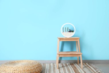 Mavi duvarın yanında dikici ve rattan pouf ile ahşap basamak.