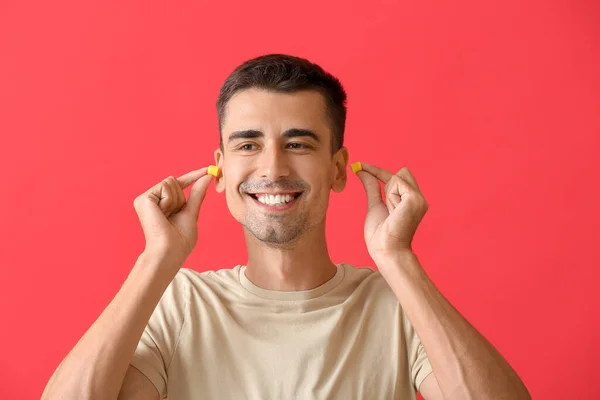 Sonriente Joven Poniendo Tapones Para Los Oídos Sobre Fondo Rojo — Foto de Stock